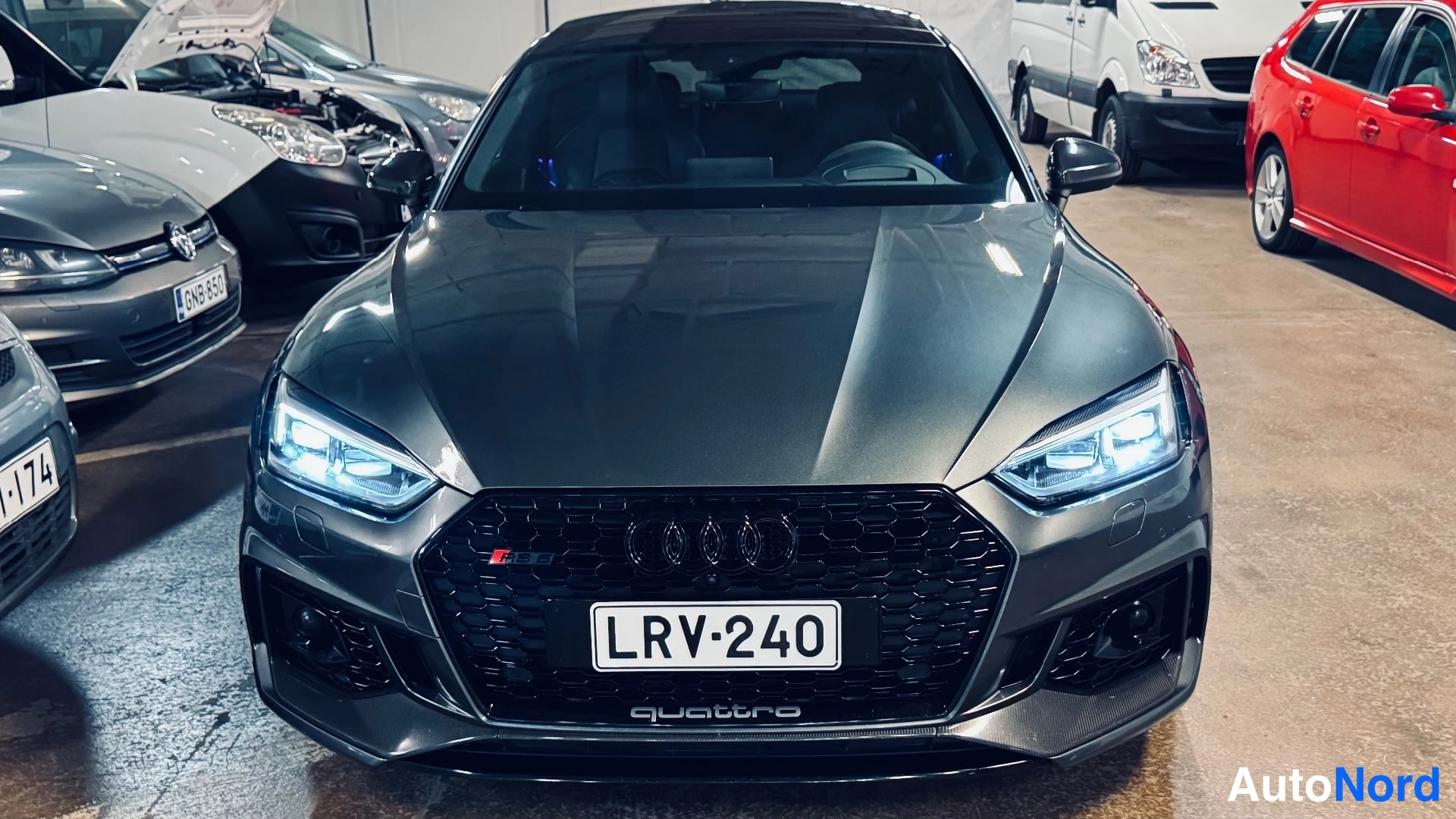 Edestä: Tummanharmaa Audi A5 Sportback edestäpäin, etumoottoritila auki, rekisteri.