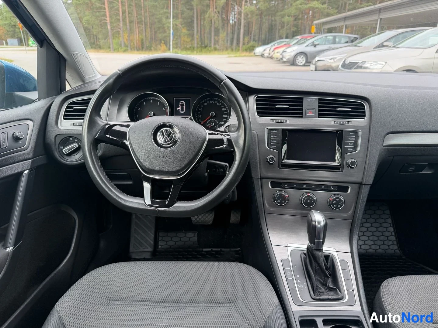 Muu: Ohjaamosta kuva: VW-ohjauspyörä, mittaristo, kosketusnäytöllinen radio ja automaattivaihteiston valitsin.