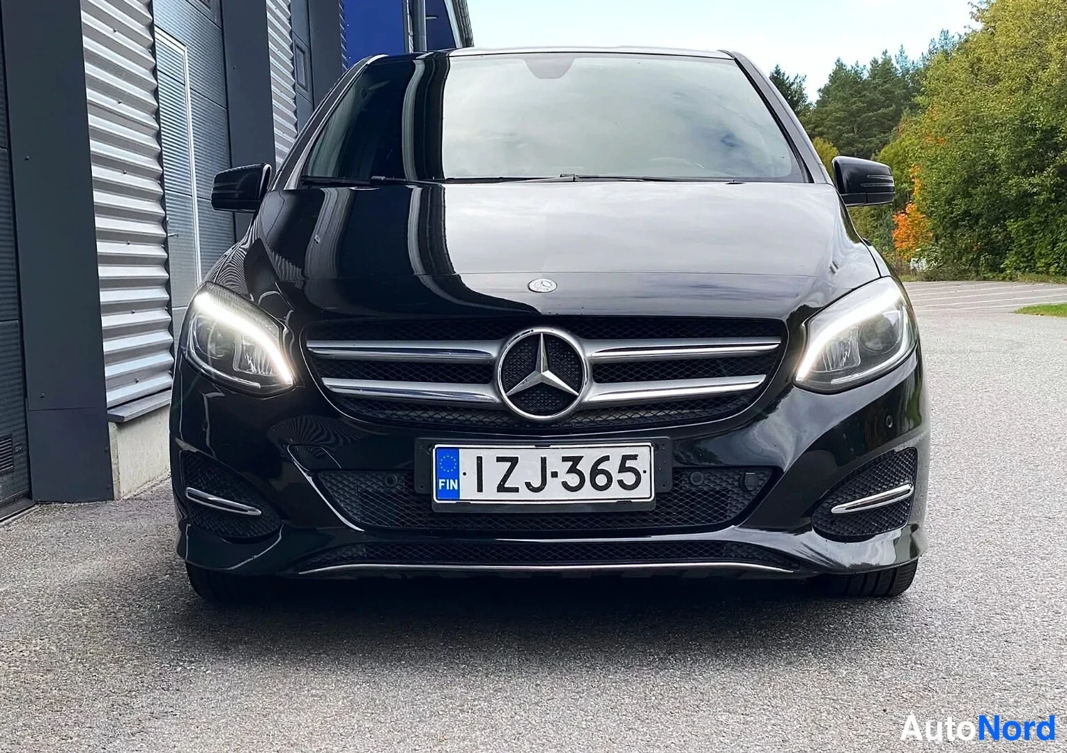 Edestä: Musta Mercedes-Benz B-sarjan auto suoraan edestä, kevyet käynnissä, rekisterikilpi.