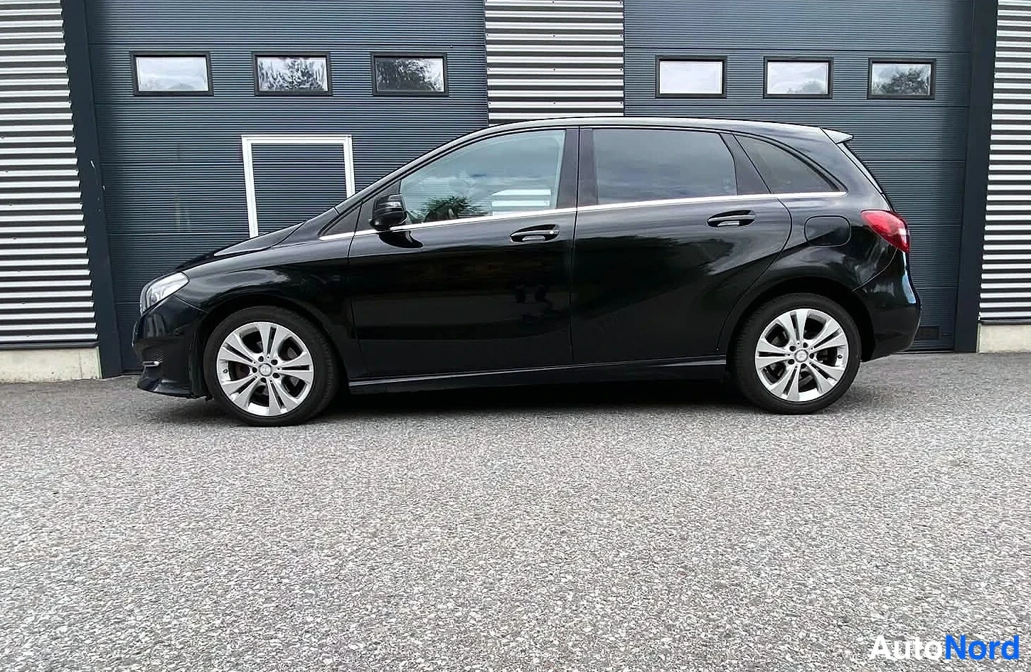 Takaviisto: Musta Mercedes-Benz B-sarjan tila-auto vasemmalta sivulta, omakätisesti autotallin edessä.