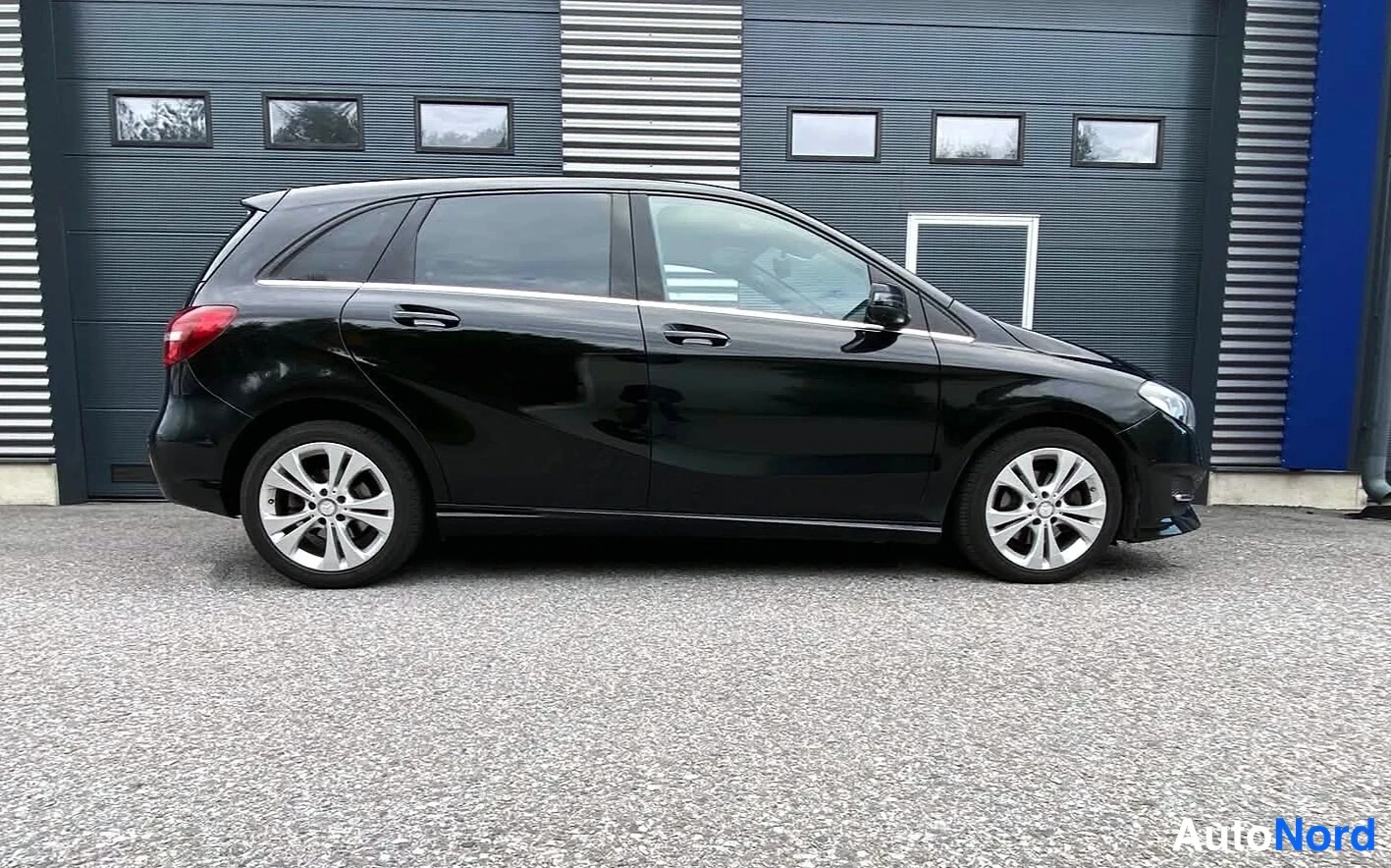 Takaviisto: Musta Mercedes-Benz B-sarja sivulta oikealta, kattotelineet ja mustat vanteet.