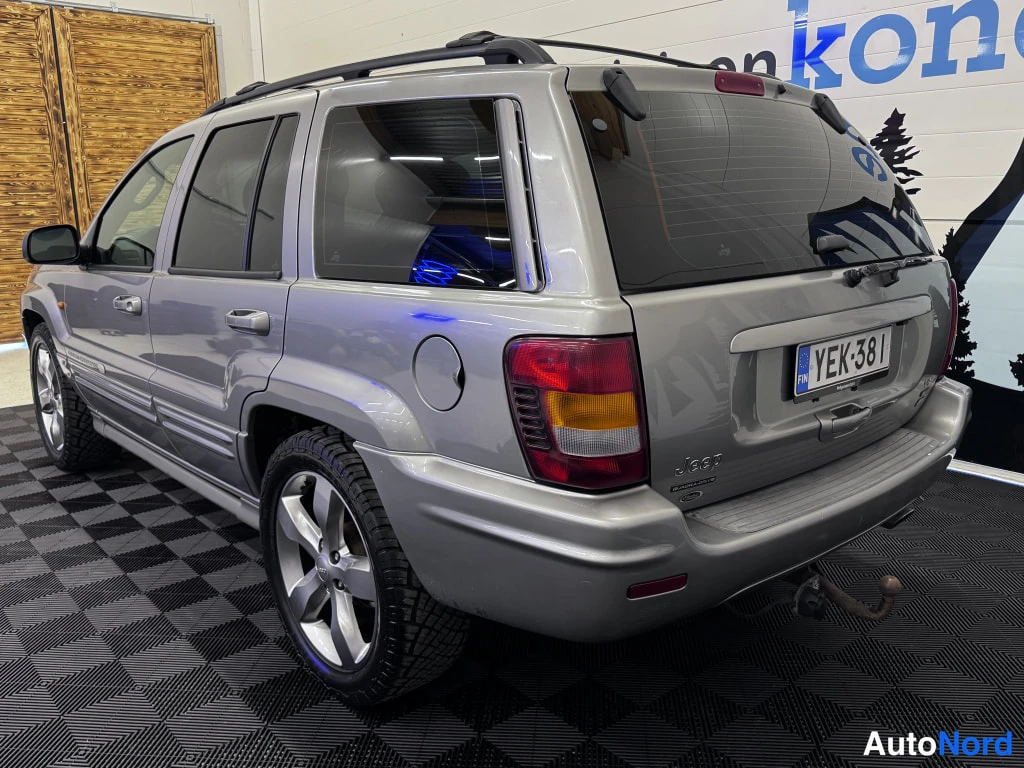 Takaviisto: Hopeanharmaa Jeep&nbsp;Grand Cherokee takaa vasemmalta kulmasta kuvattuna; rekisterikilpi, kattoteline, Jeep-merkintä ja vetokoukku näkyvissä.