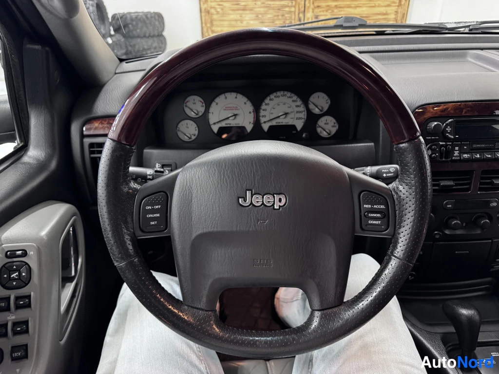 Muu: Ohjauspyörä lähikuvassa, Jeep-emblem keskellä, taustalla mittaristo ja radiopaneeli.