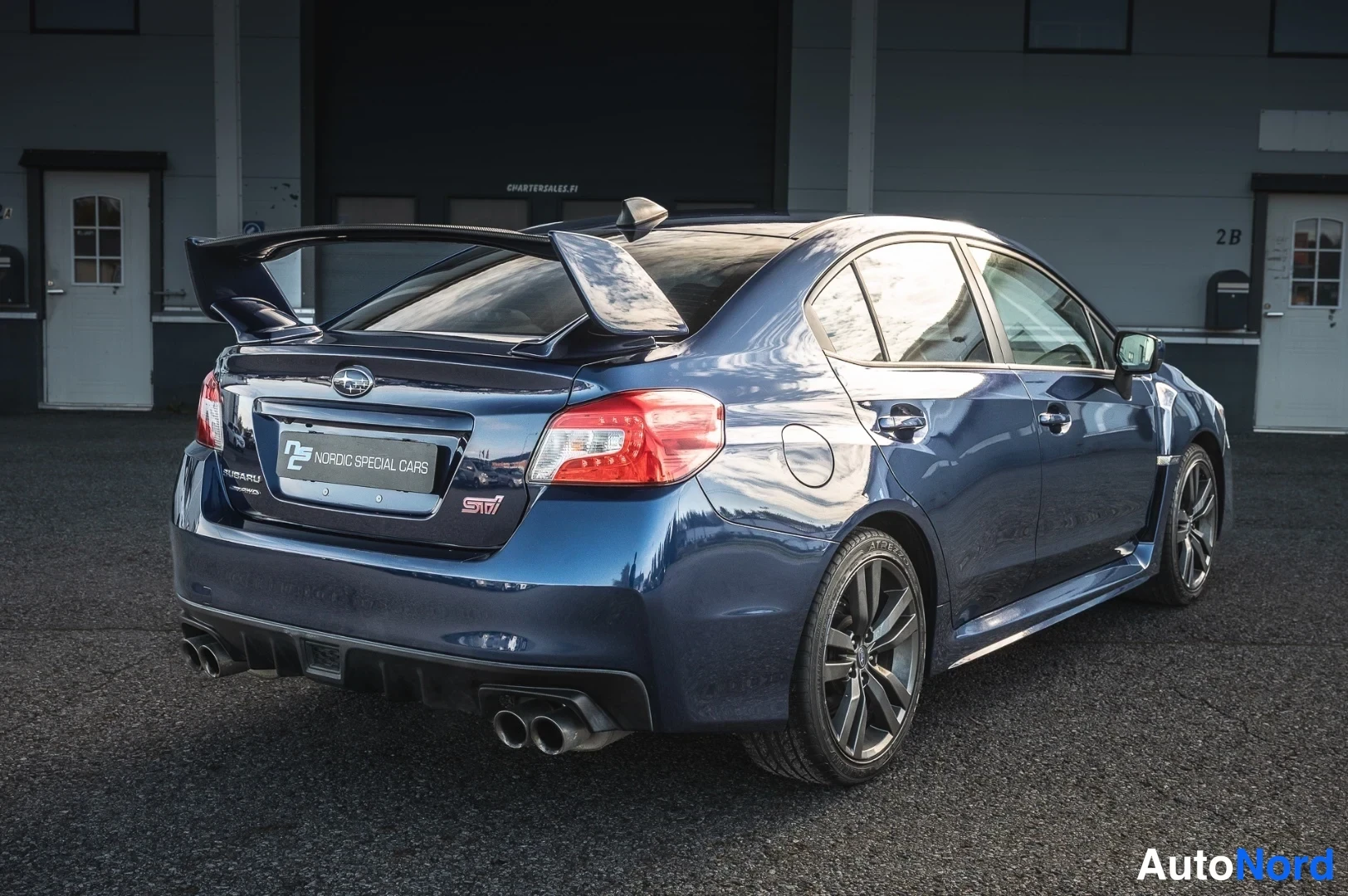 Takaviisto: Sinisen Subaru-sedan takaosa ja oikea sivu, suuri takasiipi ja neljä pakoputkea.
