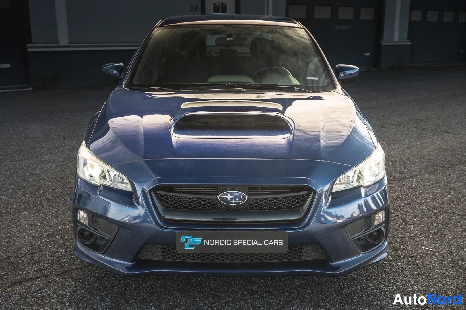 Edestä: Sininen Subaru-sedan suoraan edestä, maski ja etuvalot näkyvissä.