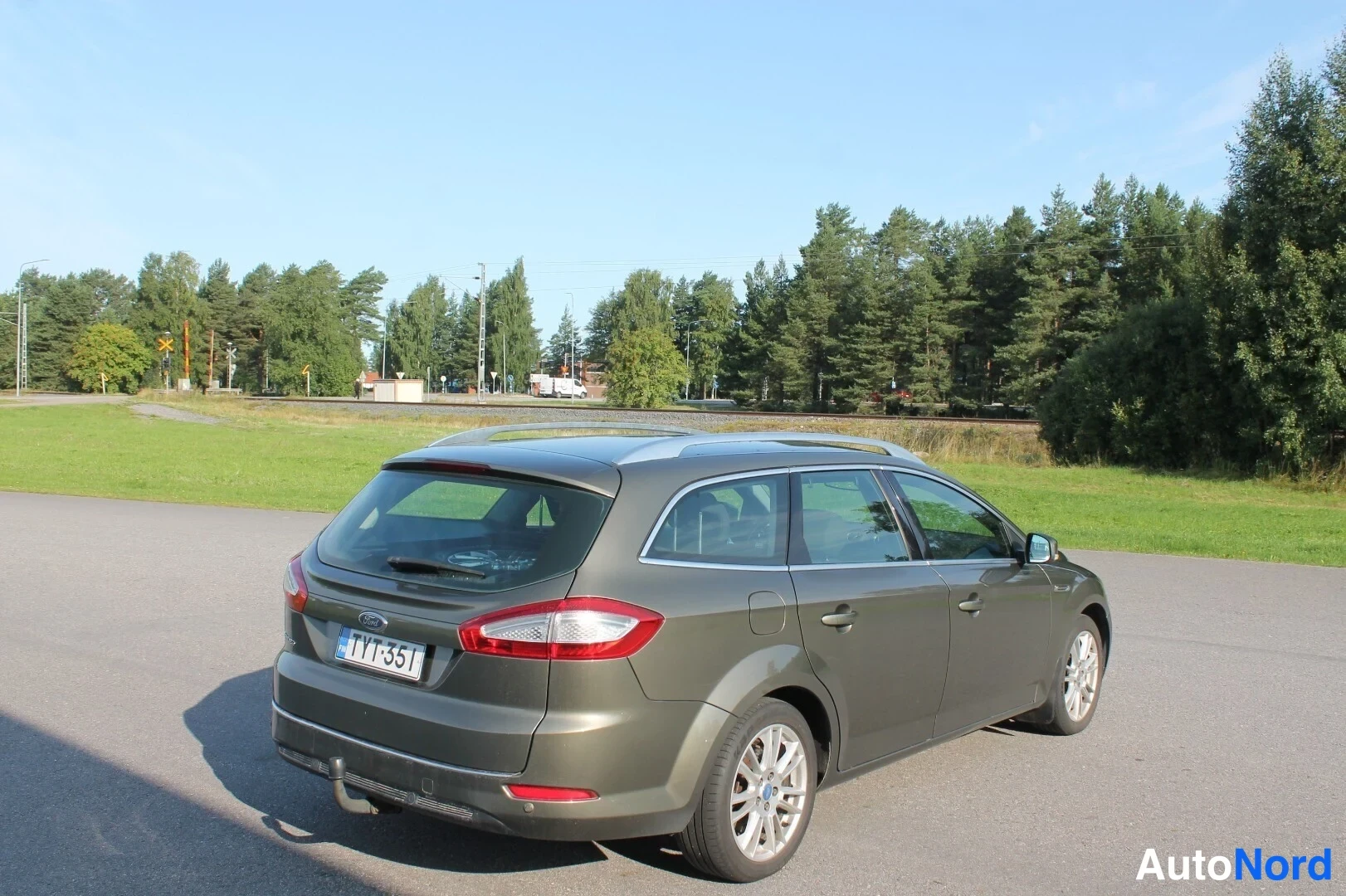 Takaviisto: Auto takaa viistosti kuvattuna pihamaalla, takana rekisterikilpi ja vetoaisa, kattokaiteet näkyvissä.