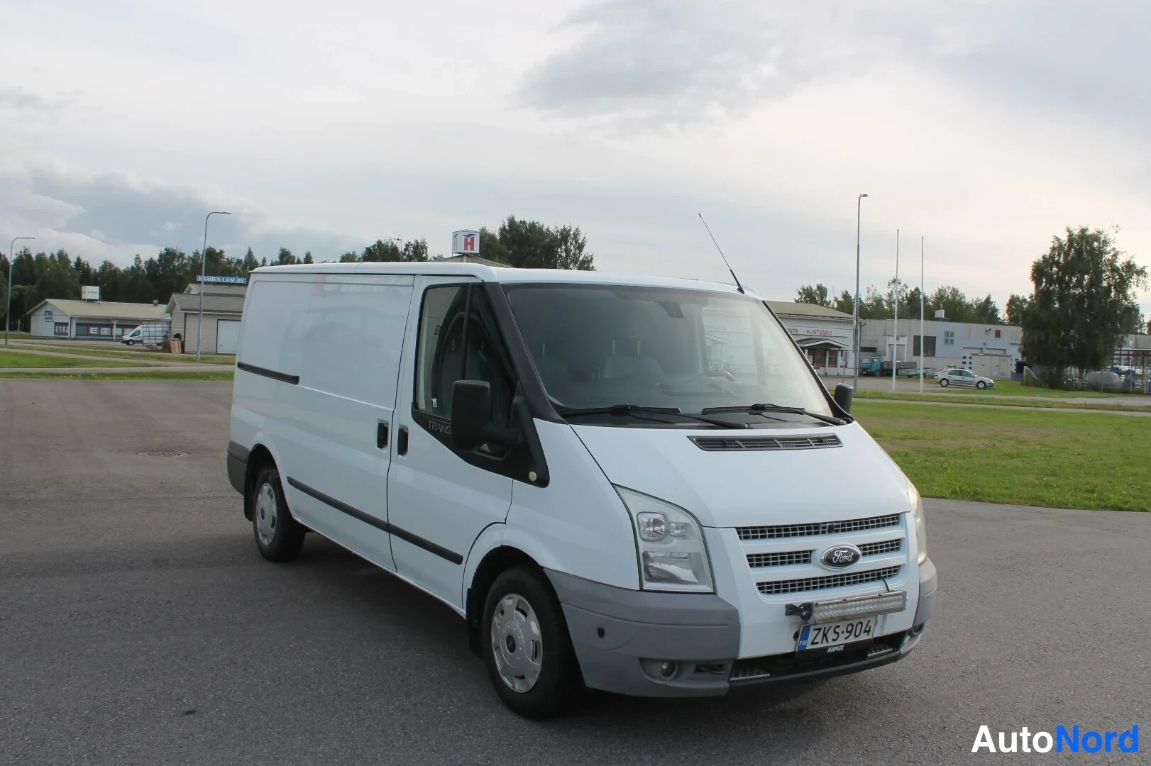 Etuviisto, nokka oikealle: Ford Transit -pakettiauton etukulmakuva oikealta, keulakulta, ajovalot ja -rekisterikilpi näkyvät.
