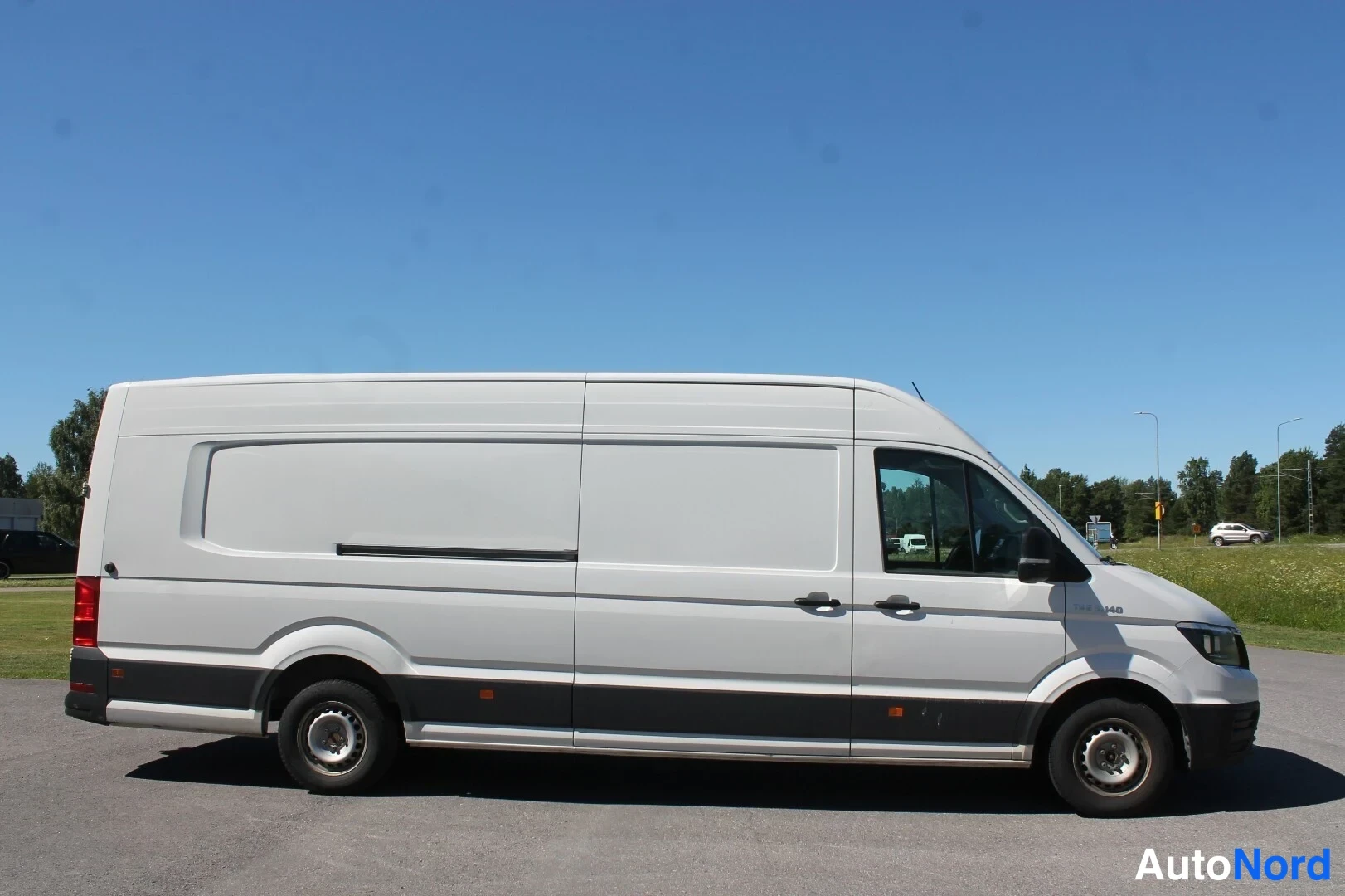 Sivulta: Valkoinen pitkä MAN-pakettiauto sivuprofiilissa, vinoovi puuttuu, taka- ja kyljessä ei lainkaan lisäikkunoita.