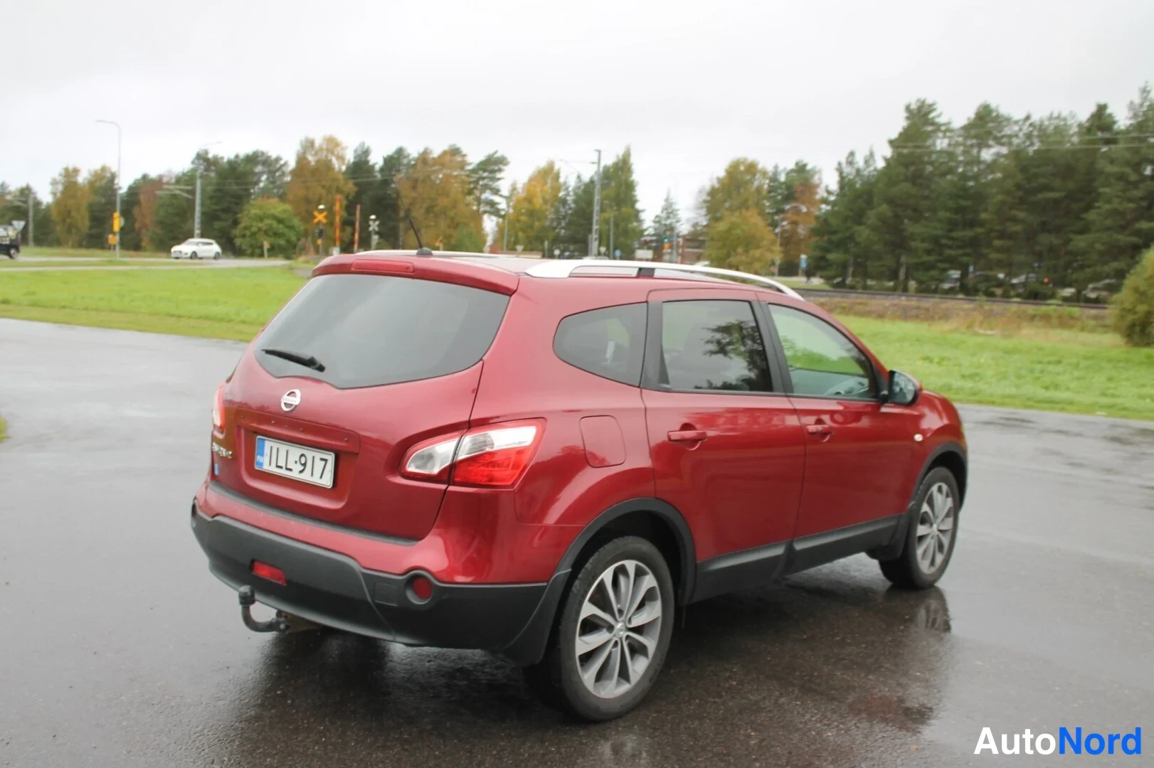 Takaviisto: Punainen Nissan Qashqai+2 takakulmasta katosta, rekisterikilpi, kattokaiteet ja vetokoukku näkyvät.