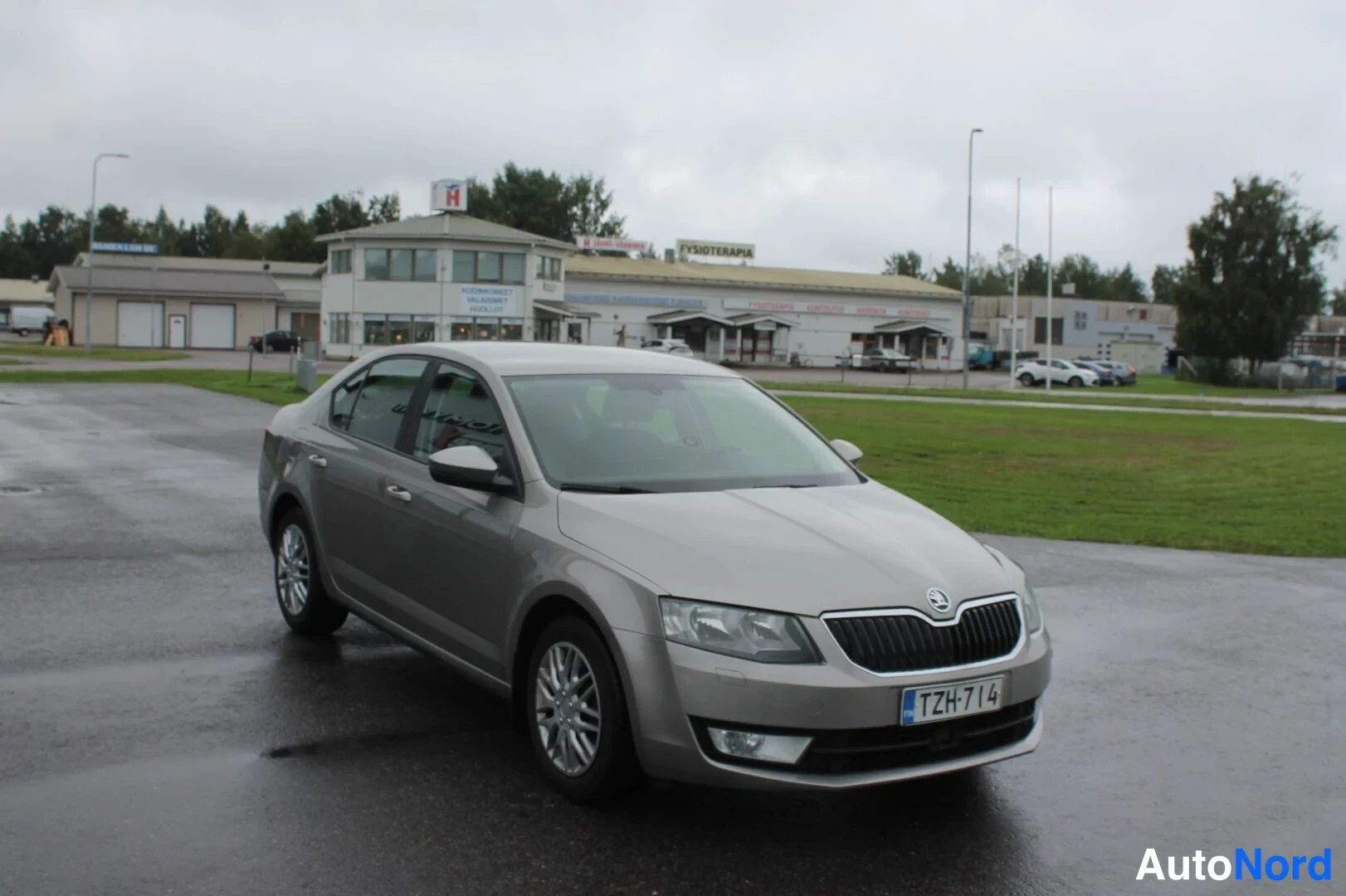 Etuviisto, nokka oikealle: Skoda Octavia -sedan etukulmasta oikealta, vaaleanbeige kori märällä parkkipaikalla.