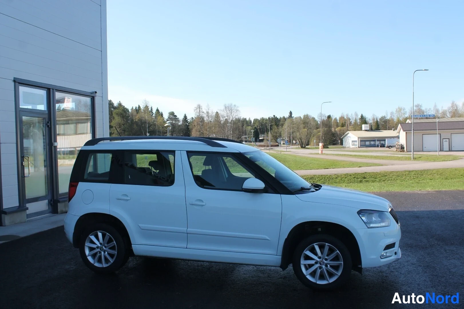 Etuviisto, nokka oikealle: Valkoinen Skoda Yeti -maasturi kuvattu kolmannelta etunurkalta, keula oikealla, katolla kattotangot ja hopeat vanteet.