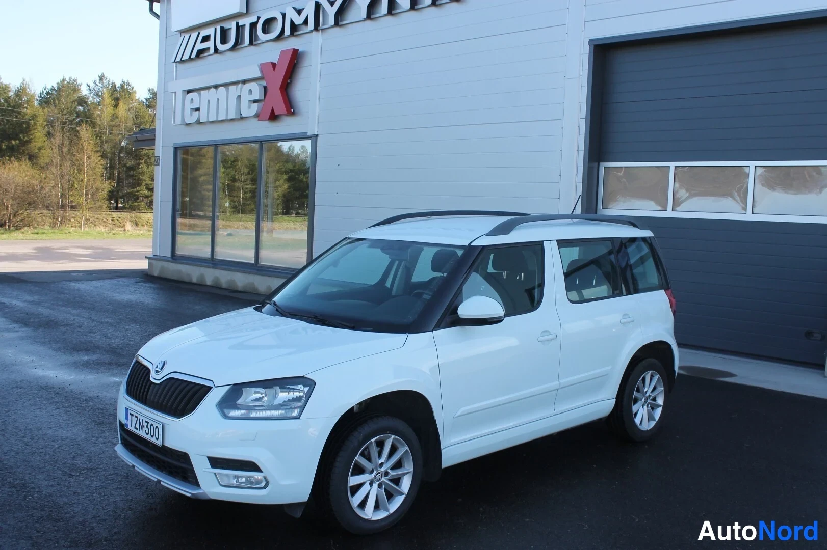 Etuviisto, nokka vasemmalle: Valkoinen Skoda Yeti taloyhtiön pihalla edestä vasemmalta kolmannelta kuvattuna, rekisterikilpi TZn-300, kattotangot asennettu.