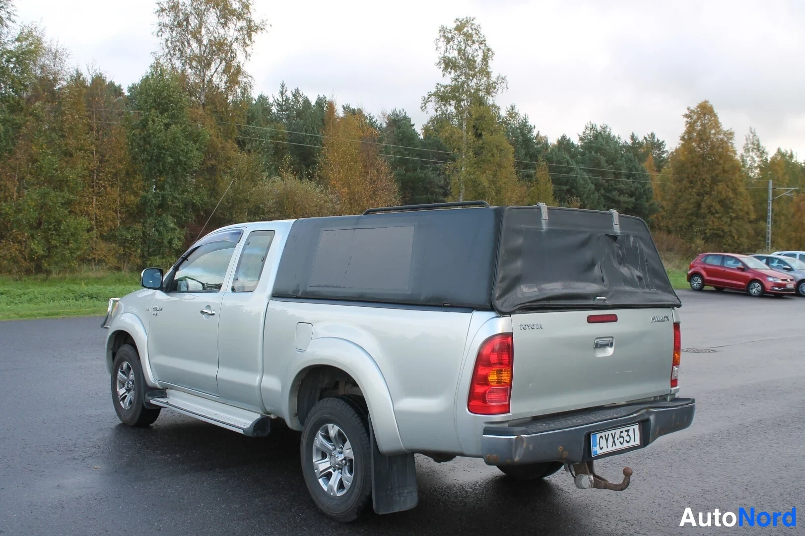 Takaviisto: Hopeanvärinen avolavakasattu pickup-kulkuauto takaviistosta kuvattuna; lavan päällä musta pehmeä kansi, rekisterikilpi ja perävaunukytkin näkyvissä.