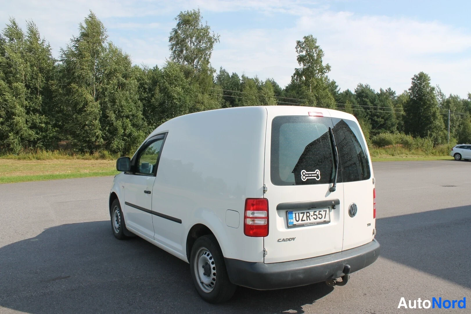 Takaviisto: Valkoinen pakettiauto takaa vasemmalta kuvattuna pysäköintialueella, rekisteritunnus, Caddy-merkintä peräovessa.