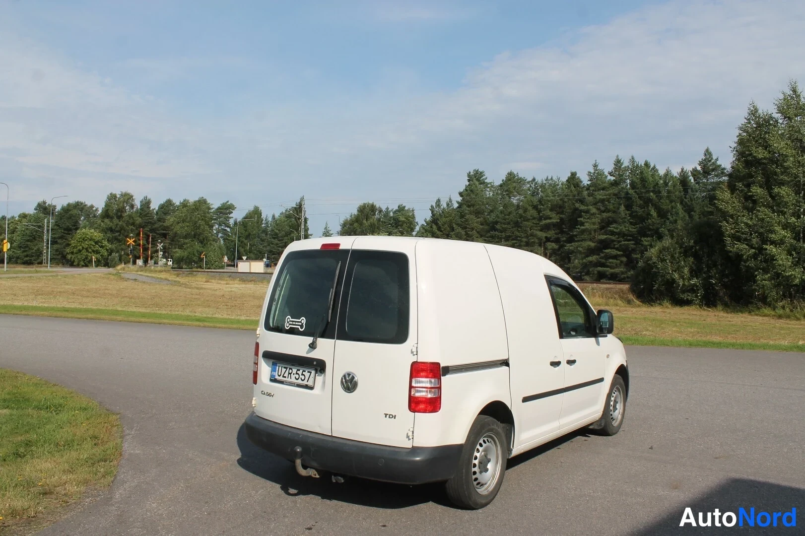 Takaviisto: Valkoinen pakettiauto takaa viistosti kuvattuna maantieympäristössä, rekisterikilpi.