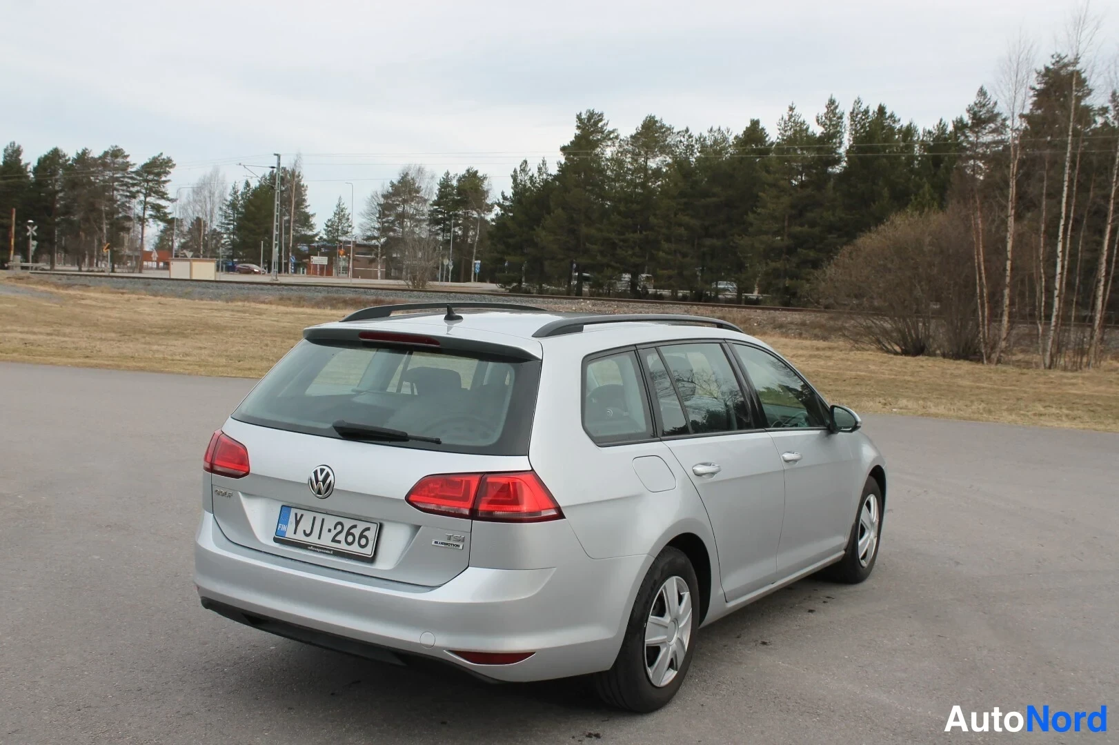 Takaviisto: Hopeinen farmariauto kuvattu takaa viistosti; takavalot, VW-merkki ja rekisterikilpi näkyvät, katolla kattokaiteet.