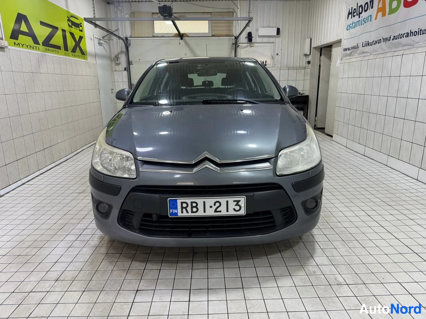 Edestä: Suora etukuva sisätilassa; tummanharmaan Citroënin etusäleikkö, ajovalot ja rekisteri näkyvissä.