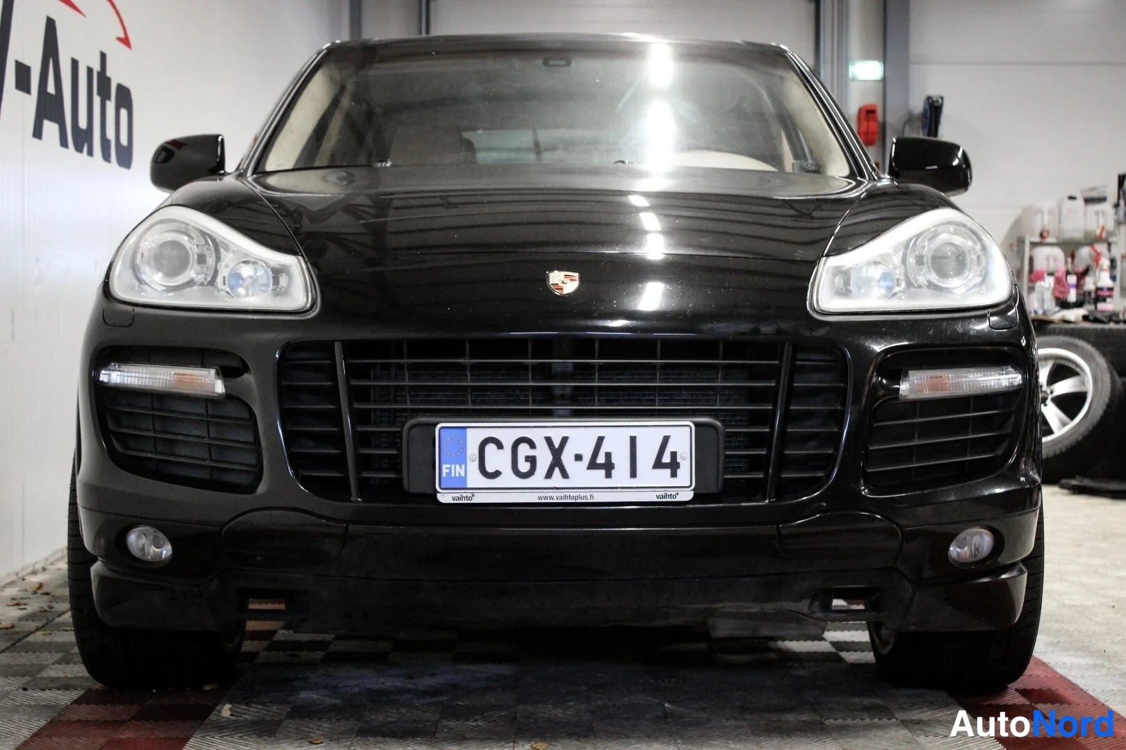 Edestä: Mustan Porsche Cayennen etunäkymä suoraan edestä, suuret ajovalot, musta etusäleikkö ja rekisteritunnus.