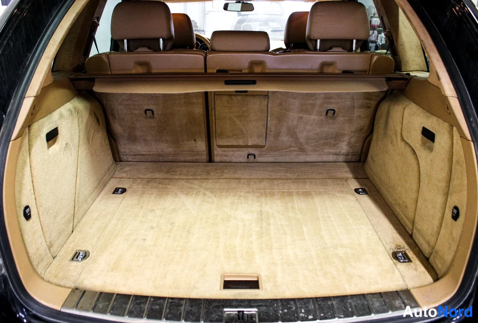 Muu: Porsche Cayennen avattu tavaratila, beige carpet ja taitettu penkkien selkänojat.