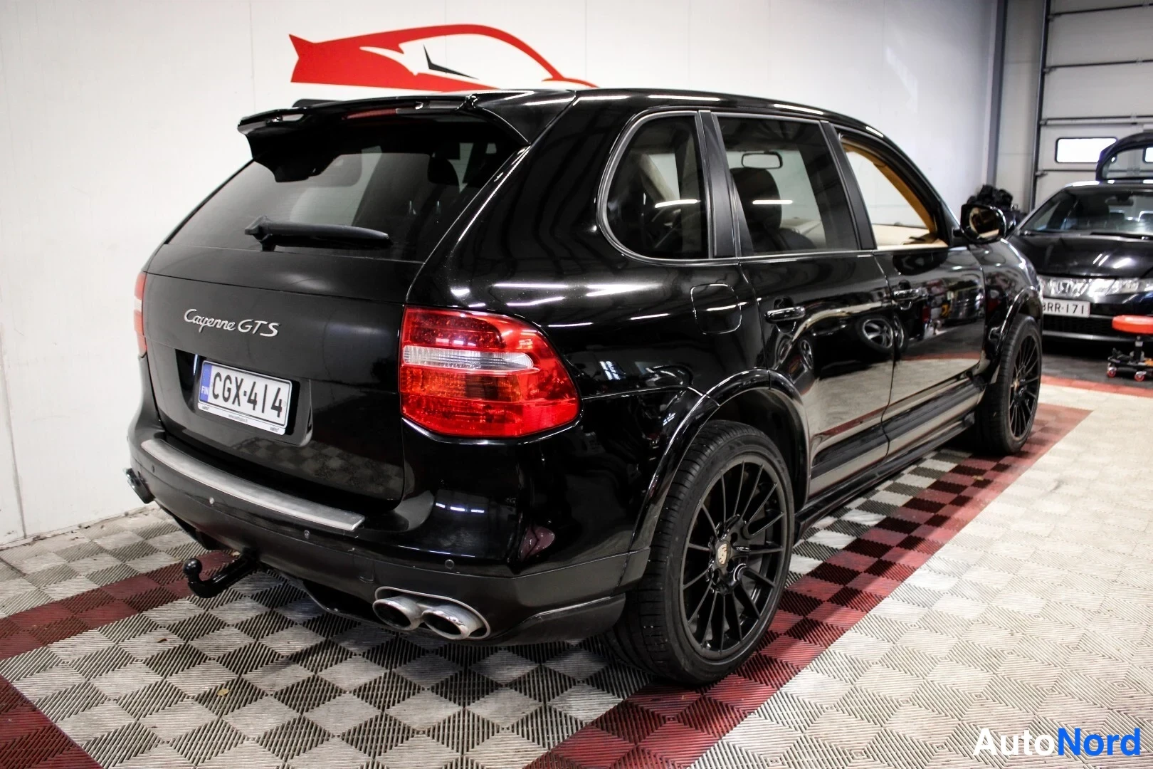 Takaviisto: Porsche Cayenne GTS:n takaosasta ja vasemmasta kyljestä kuvattu musta auto hallissa; takana spoileri, kaksi pakoputkea ja luku.