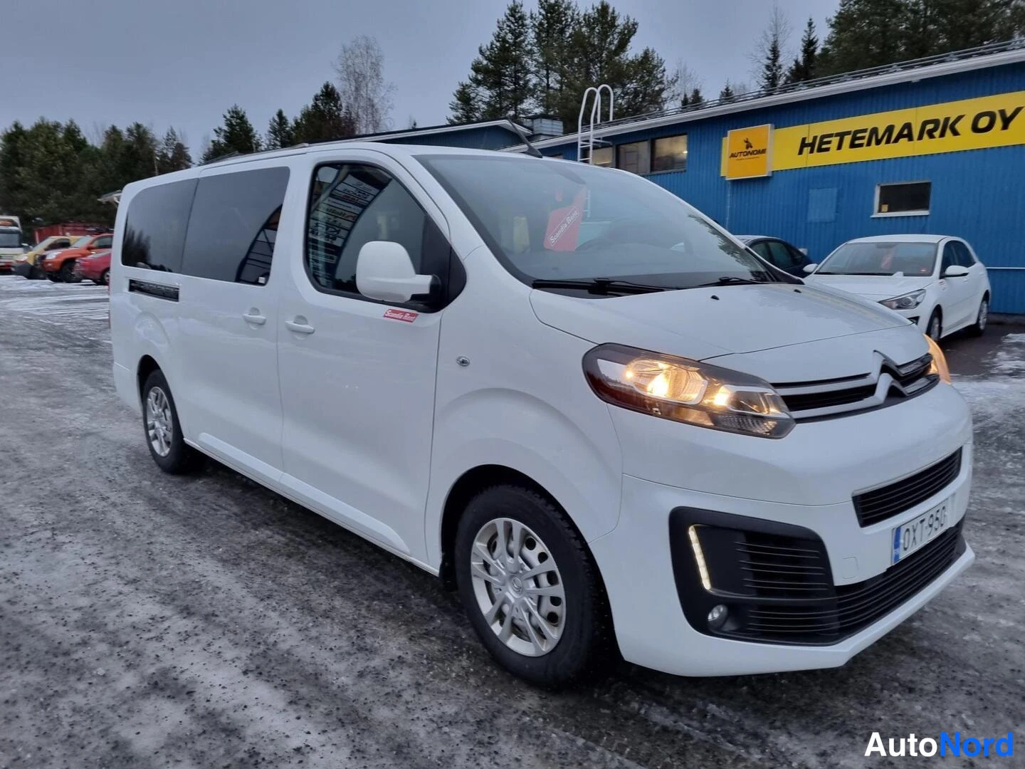 Etuviisto, nokka oikealle: Valkoinen Citroën -pakettiauto neljännesnäkymässä edestä oikealta, ajovalot päällä, rekisterikilpi.