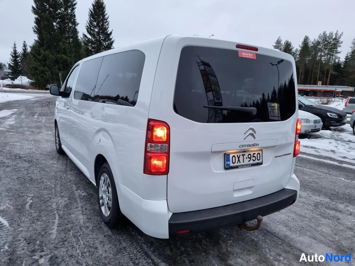 Takaviisto: Valkoinen Citroën -pakettiauto kuvattu takaa viistosti, rekisterikilpi, takavilkut palavat, lumisella parkkipaikalla.