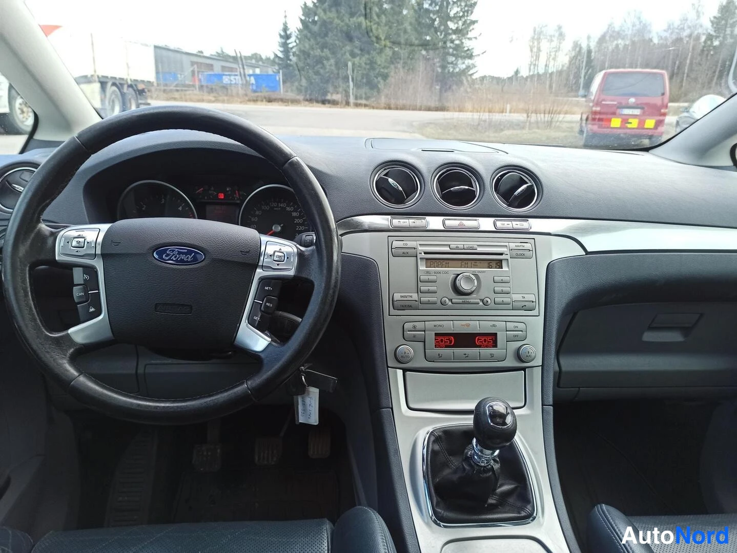 Muu: Ford S-MAXin kojelauta ja ohjauspyörä edestä: kolme pyöreää ilmastointisuutinta, radiopaneeli ja manuaalivaihteen keksi keskikonsolissa.