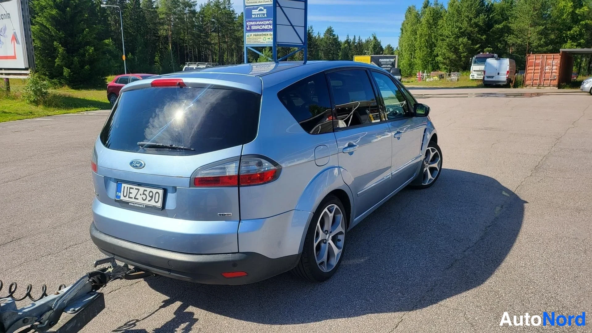 Takaviisto: Sinisen Ford S-MAX:n takakulma tienoolta, takavaloissa ja rekisterikilvessä teksti.