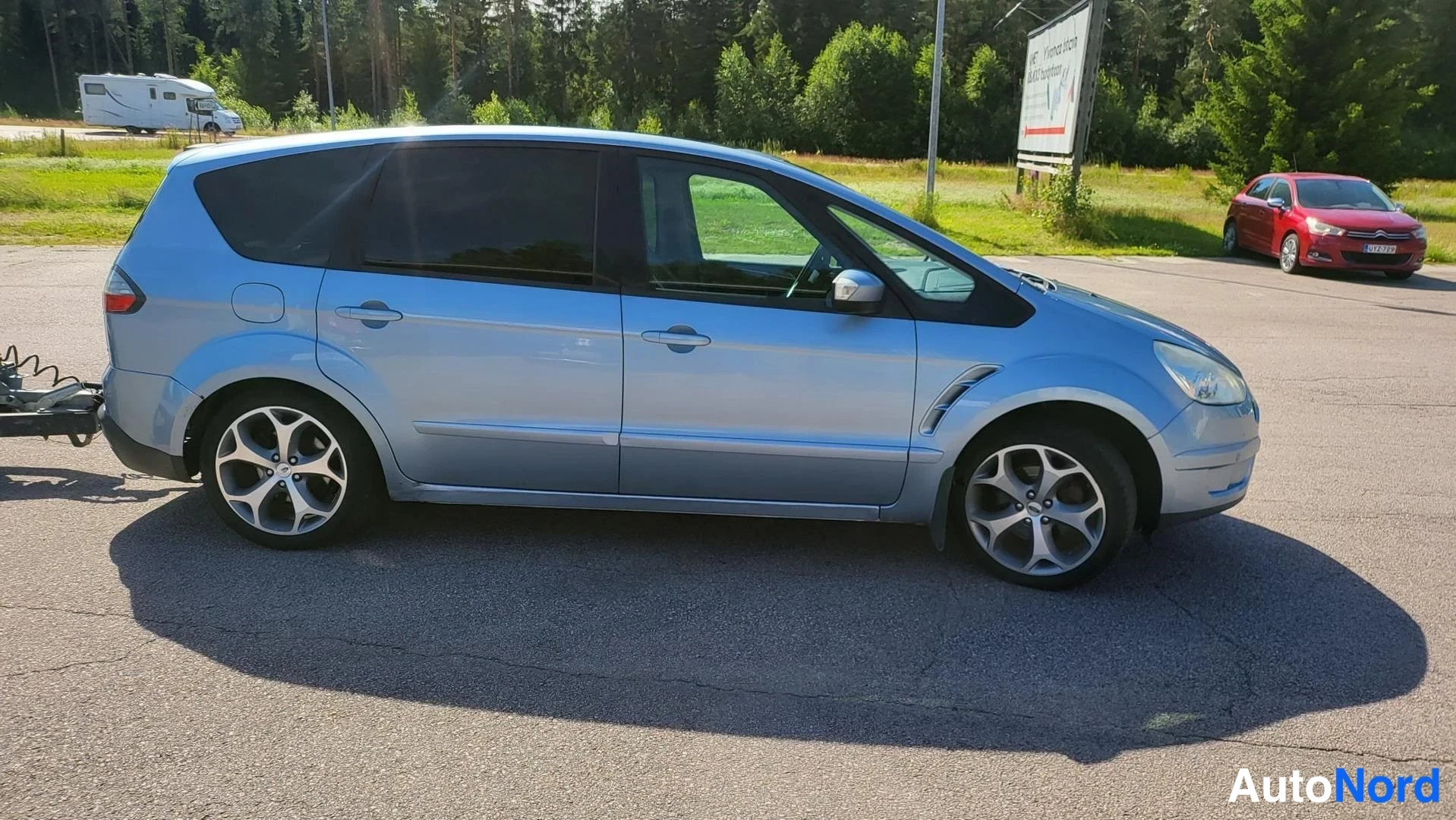 Etuviisto, nokka oikealle: Vaaleansininen Ford S-MAX etsen kylkikuvassa, keula näkyy kulkuaian oikealla puolella.