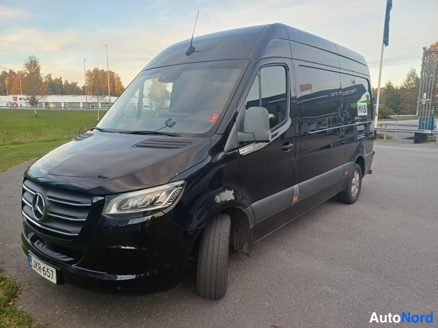 Etuviisto, nokka vasemmalle: Musta Mercedes-Benz Sprinter -pakettiauto etuviistöstä vasemmalta, rekisterikilpi.