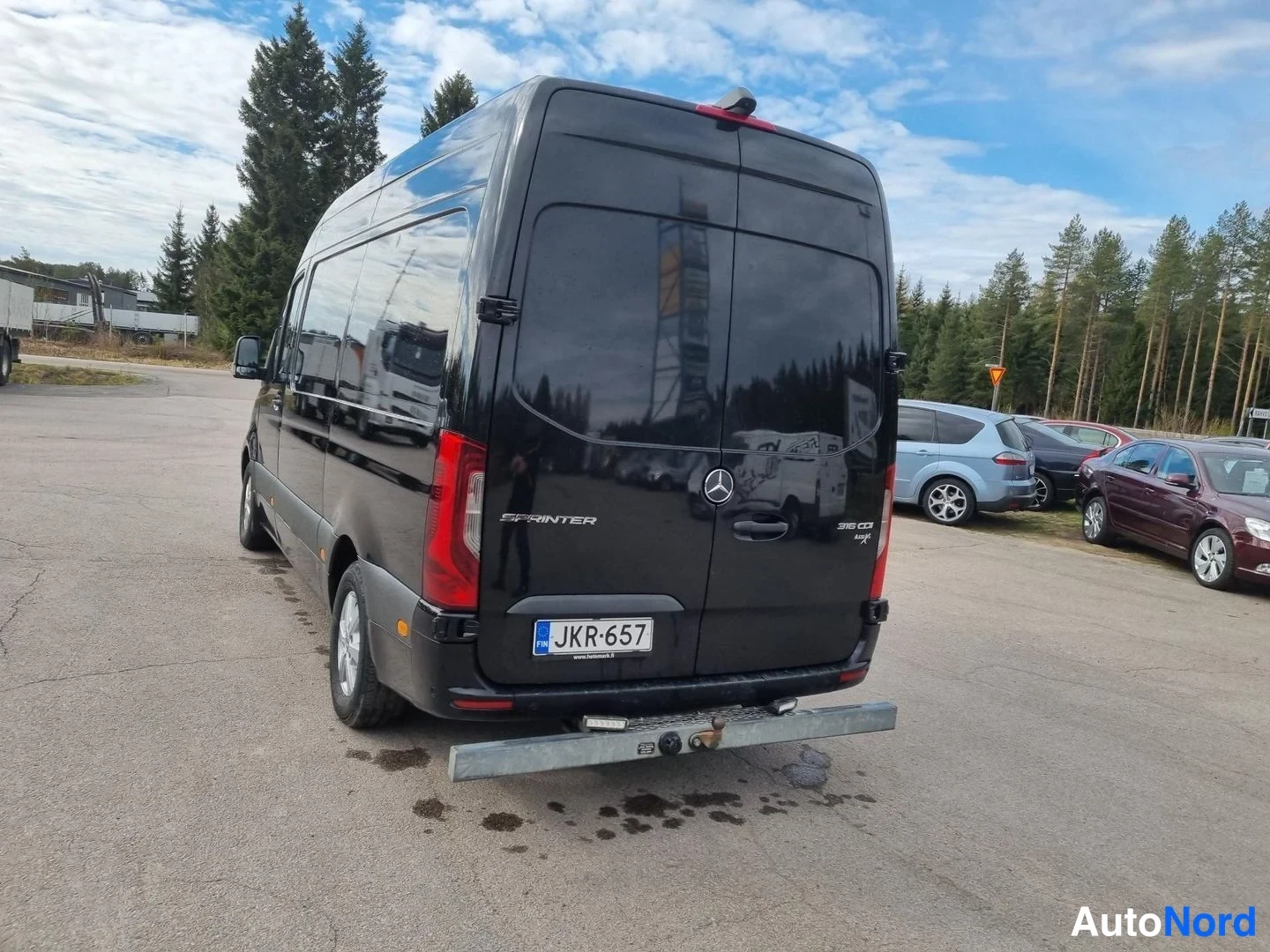Takaviisto: Musta Mercedes-Benz Sprinter -pakettiauto takaviistosta, takapää ja vasen kylki näkyvissä.
