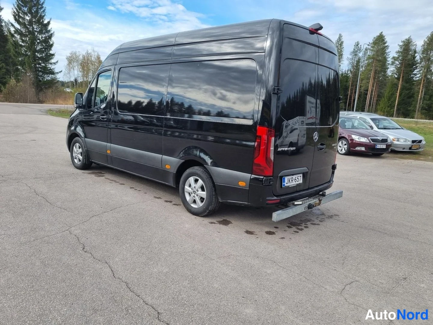 Takaviisto: Musta Mercedes-Benz Sprinter -pakettiauto takaviistosta, kylki ja takaosa näkyvissä, vetokoulu takana.