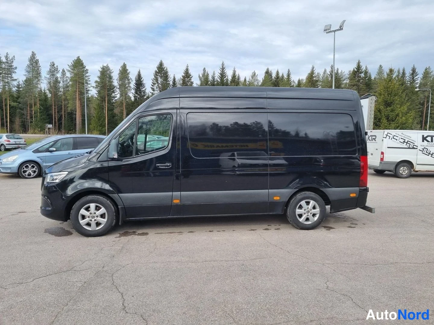 Etuviisto, nokka vasemmalle: Musta Mercedes-Benz -pakettiauto sivulta etukulmasta, keula vasemmalla.