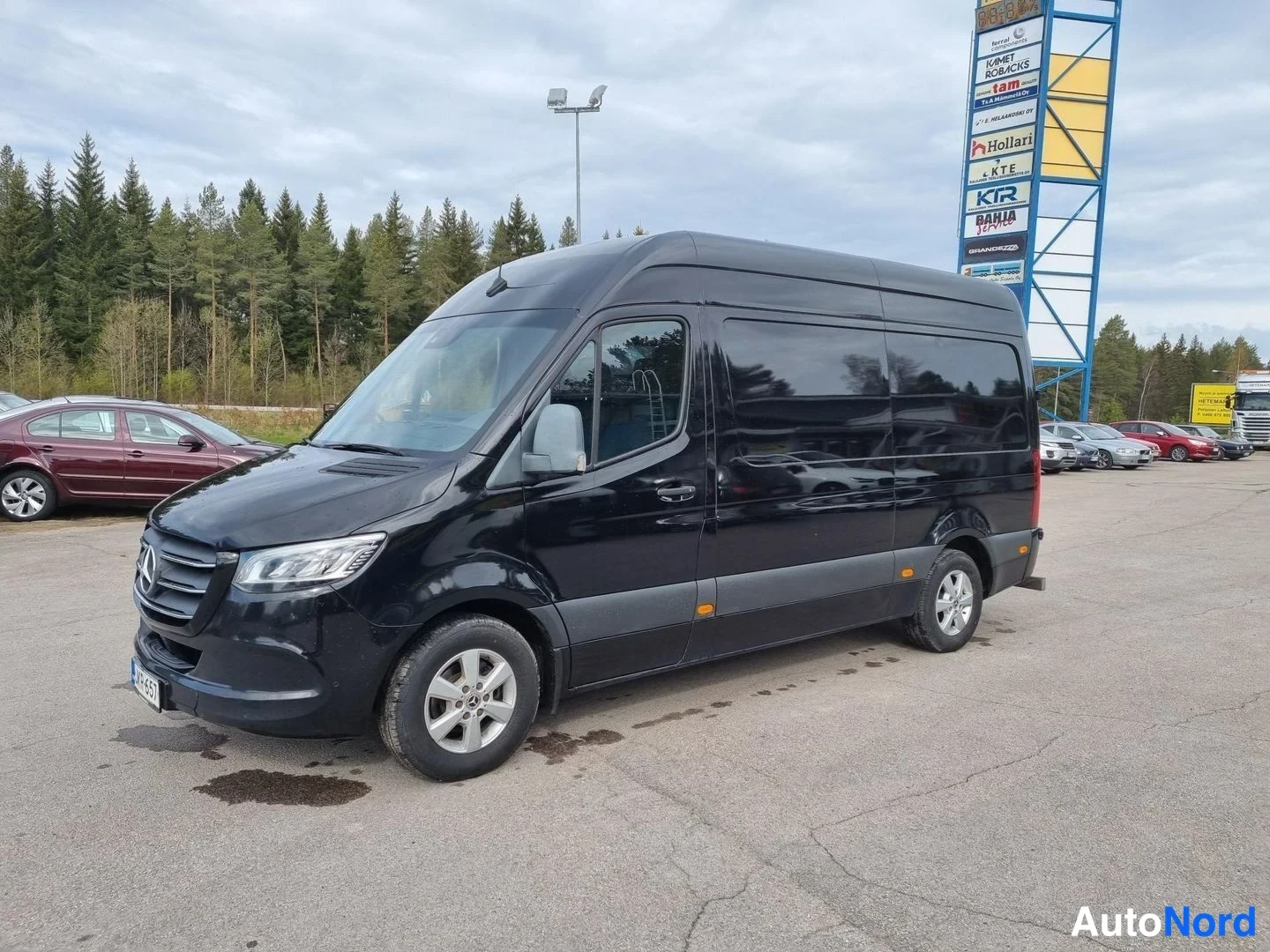 Etuviisto, nokka vasemmalle: Musta Mercedes-Benz -pakettiauto etukulmasta, keula vasemmalla.