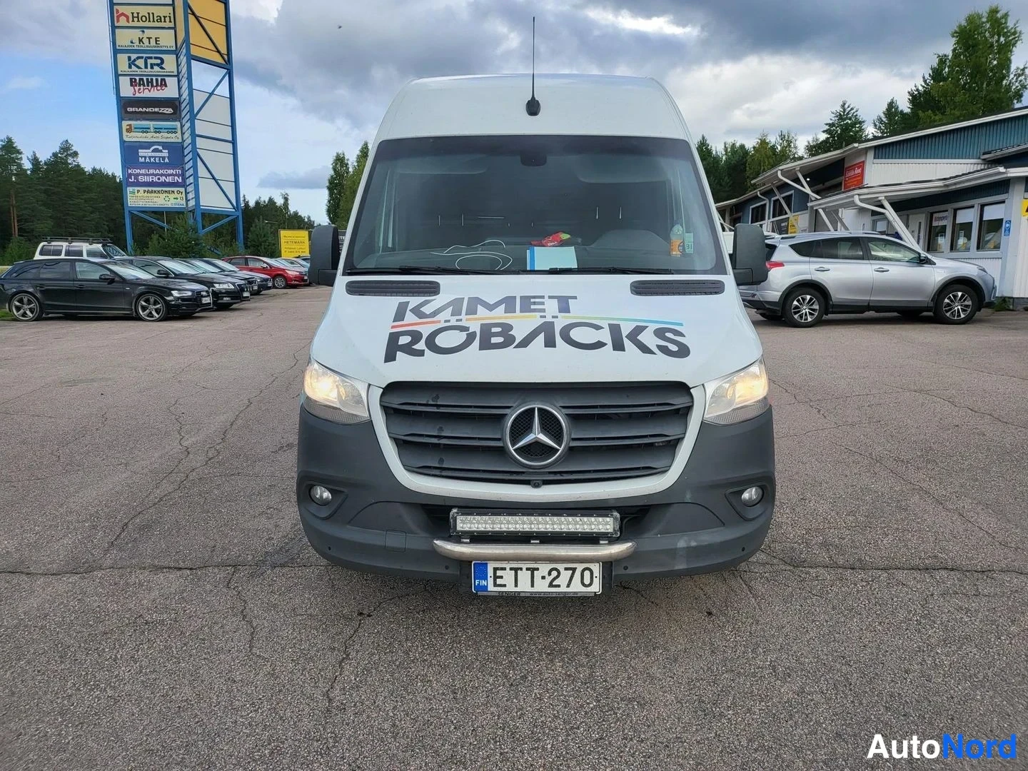 Edestä: Mercedes-Benz Sprinter -pakettiauto suoraan edestä valkoisena, konepellissä KAMET RÖBÄCKS-teksti.