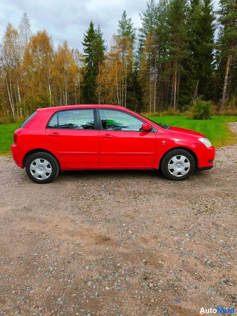 Etuviisto, nokka oikealle: Punaisen Toyota Corolla -viistoperän sivuprofiili sorapohjalla, mukana etuosa ja takavalo lievästi kulmasta.