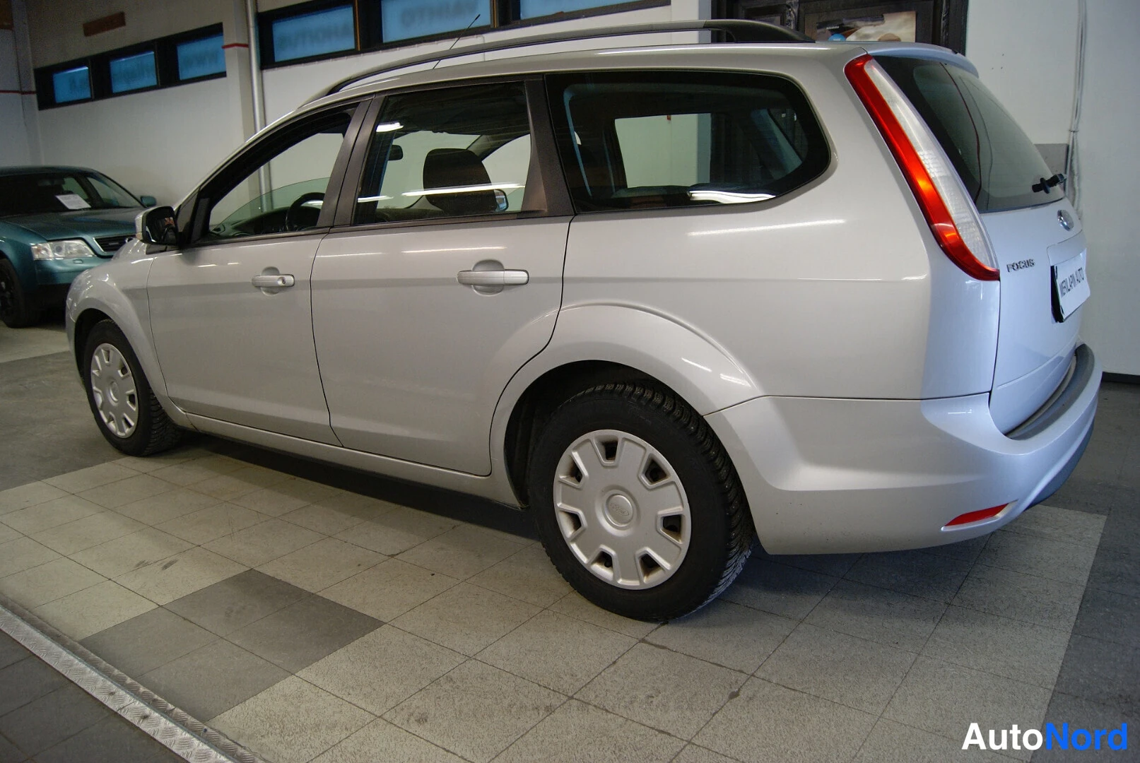 Takaviisto: Ford Focus Farmari 2008, hopeanvärinen, kulmakuva takaa vasemmalta; takavalot, takaluukku ja kylki näkyvissä.