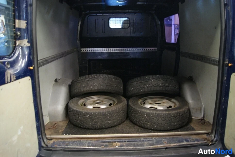 Muu: Avoimen tavaratilan sisäkuva; lattialla pinottuna neljä talvirengasta vanteineen, oven reunissa pintaruostetta.