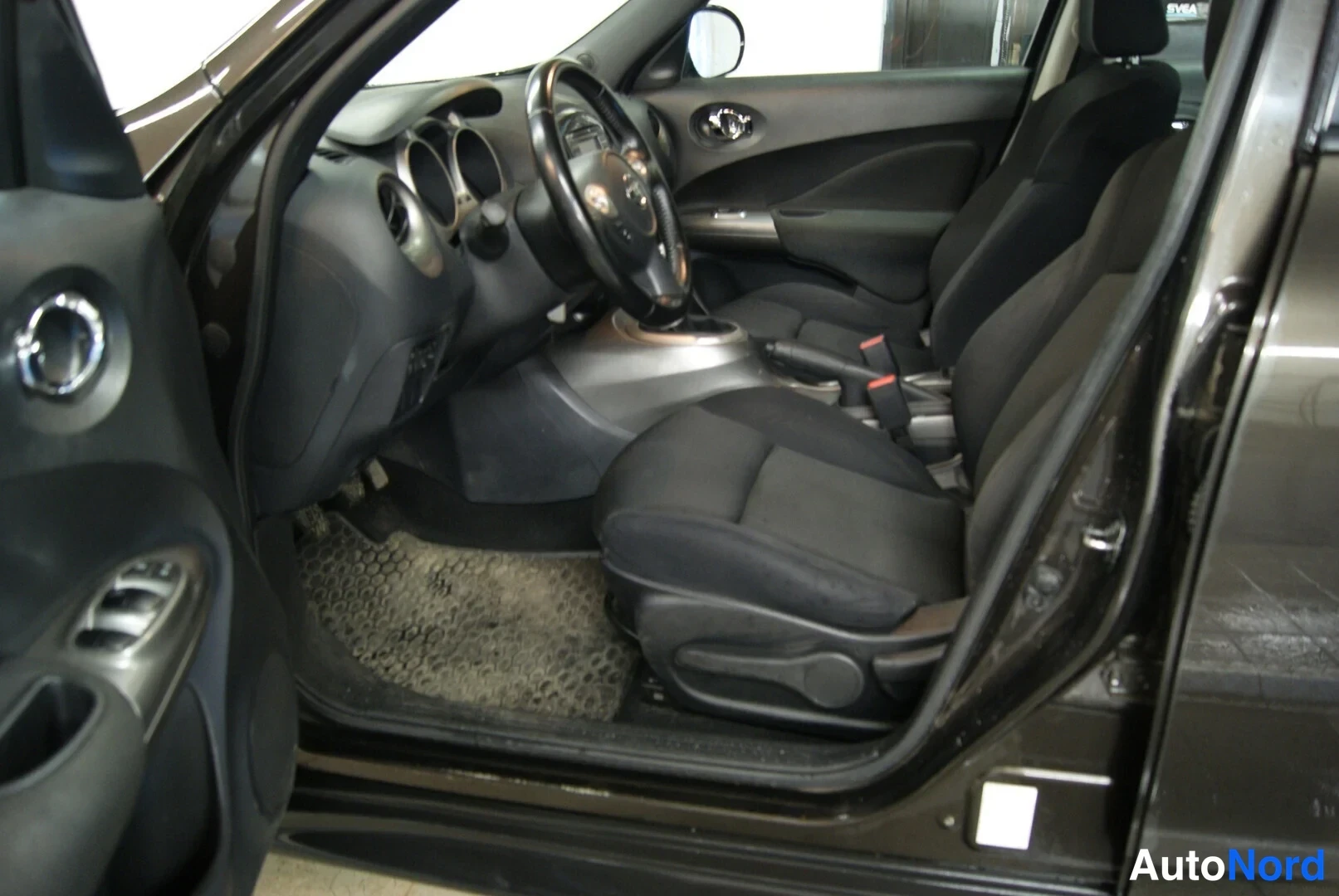 Sivulta: Nissan Juken etumatkustamo kuljettajan ovesta katsottuna, tummat penkit ja kojelauta.