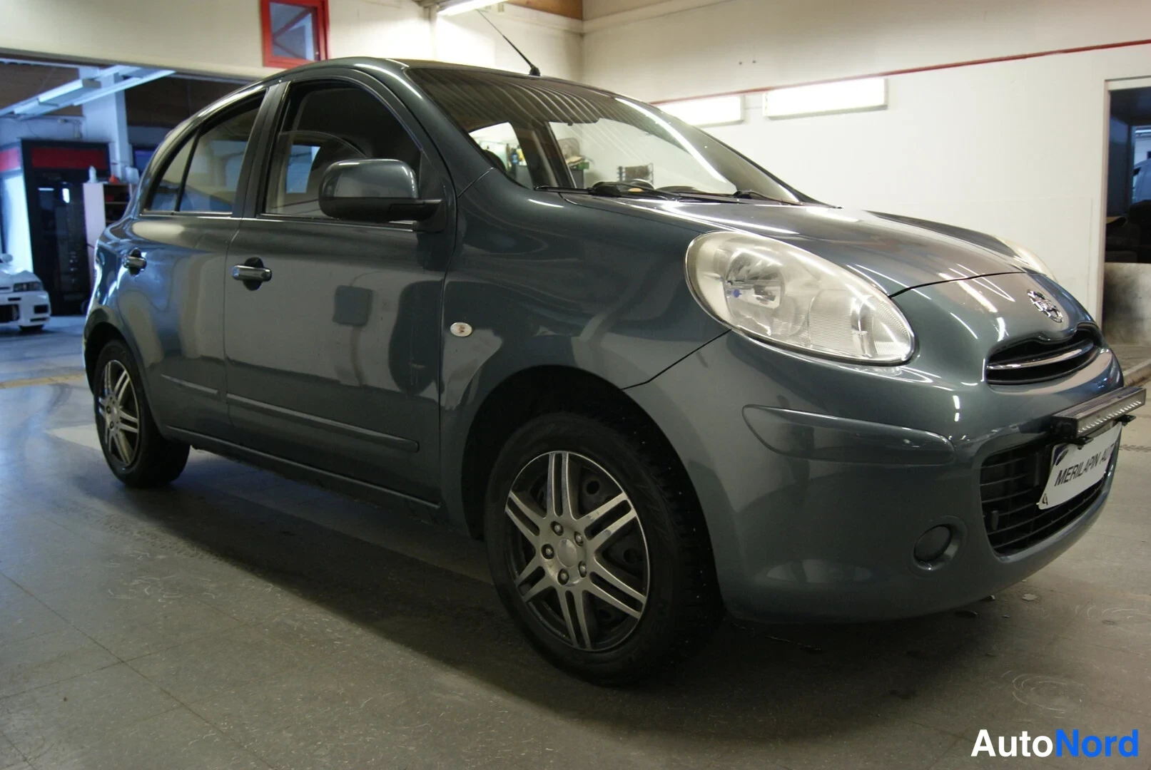 Etuviisto, nokka oikealle: Tummanharmaa Nissan Micra edestä oikealta kuvattuna autotallissa