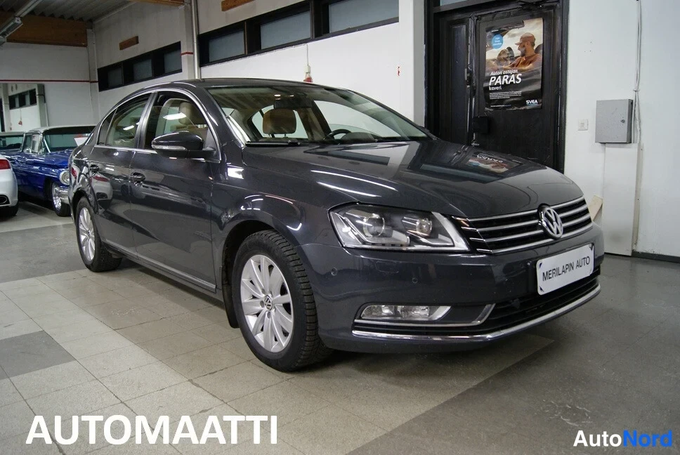 Etuviisto, nokka oikealle: Tummanharmaan Volkswagen Passat -sedanin etukulmanäyttö myyntihallissa.