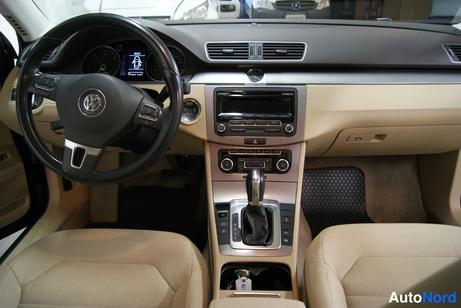 Edestä: Volkswagenin ohjaamo: beige sisusta, monitoimiohjauspyörä, radio ja automaattivaihteen valitsin.