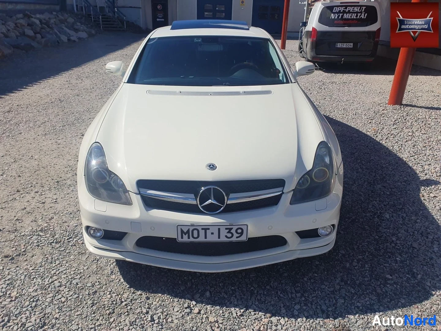 Edestä: Valkoisen Mercedes-Benz CLS:n keula suoraan edestä, Mercedes-tähti etusäleikössä ja rekisterikilpi.