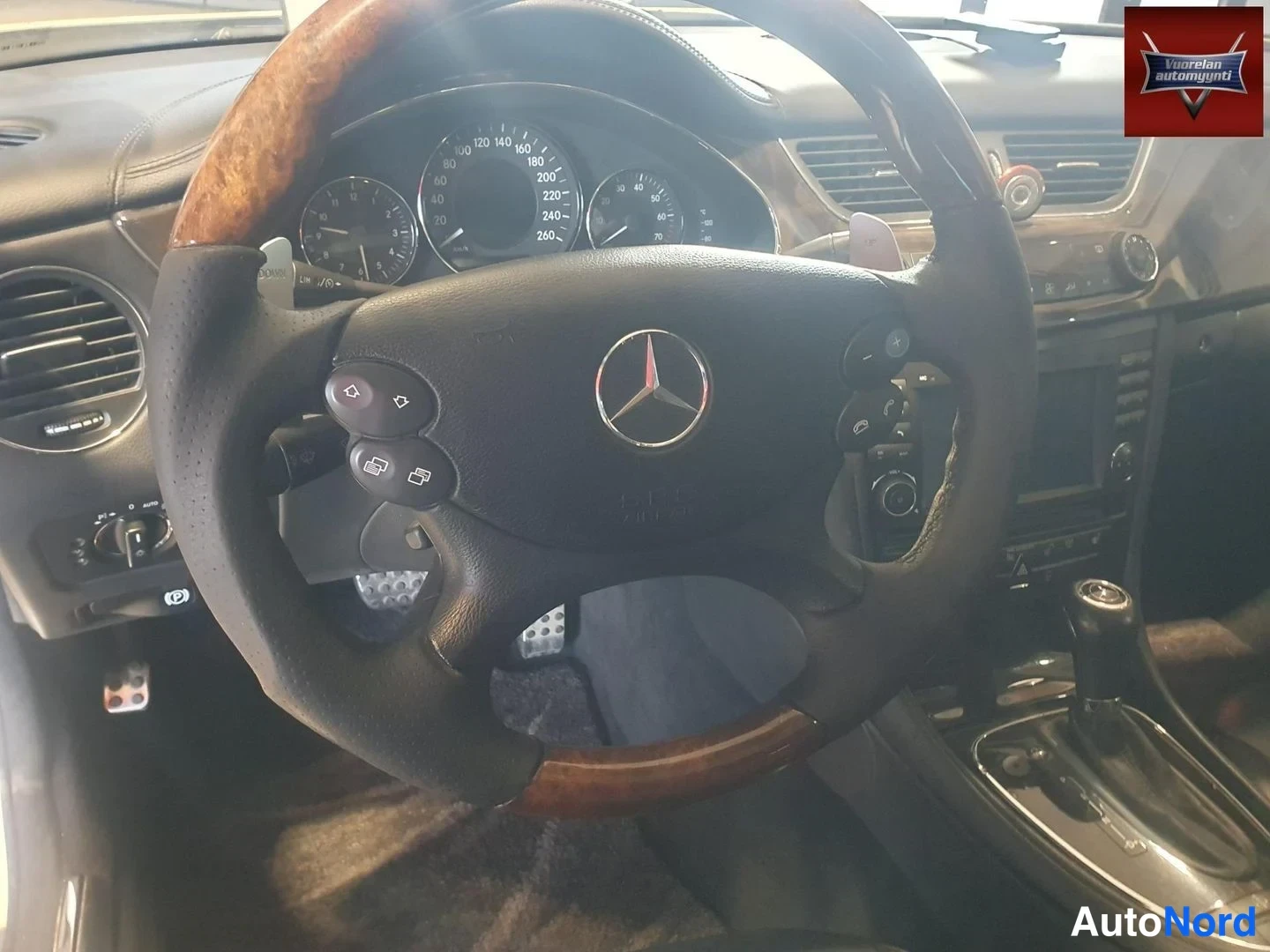 Muu: Ohjaamosta kuva: Mercedes-tunnuksella varustettu puupintainen ohjauspyörä, mittaristo ja keskikonsoli.