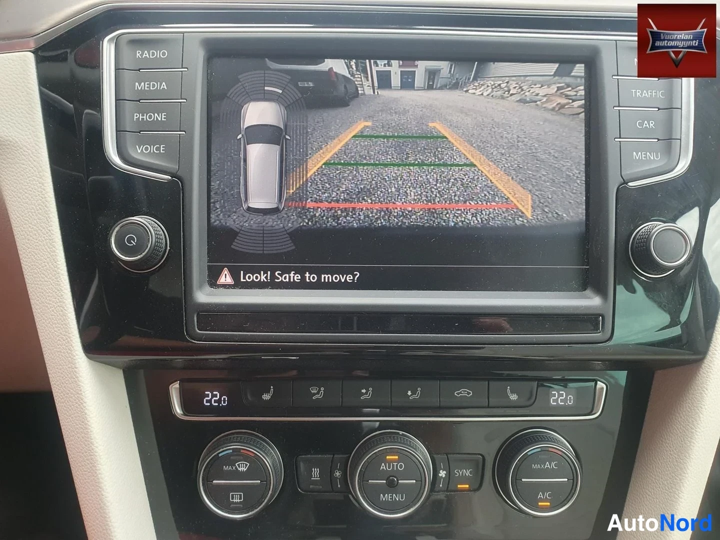 Muu: Auton keskikonsoli: infotainment-näytöllä peruutuskameran kuva parkkioppaaviivoineen ja teksti 'Look! Safe to move?', alla kaksivyöhykeinen automaatti-ilmastoin