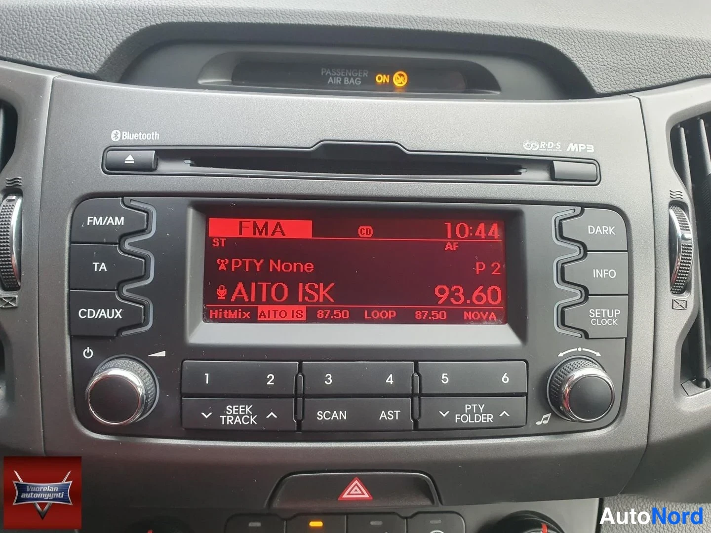 Yksityiskohta: Auton keskitunnelin radiopaneeli: näytöllä radiokanava 93.60, nimi AITO ISK ja kello 10:44; paneelissa Bluetooth-merkintä, CD-aukko sekä RDS- ja MP3-merkinnot.