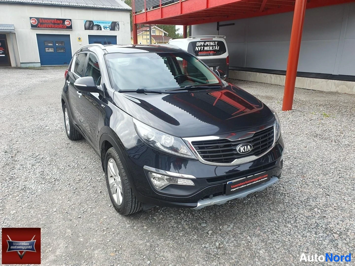 Etuviisto, nokka oikealle: Musta Kia Sportage kuvattu kolmanneltä etunurkaltaan, etusäleikko ja ajovalot näkyvät.
