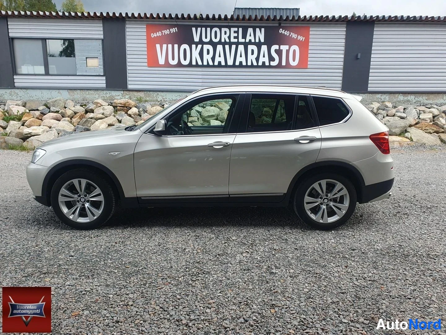 Takaviisto: BMW X3:n takakulman sivukuva, auton beige-karmaiseen kori ja kevytmetallivanteet näkyvät hiekkapohjaisella pihalla vuokra-varaston edessä.