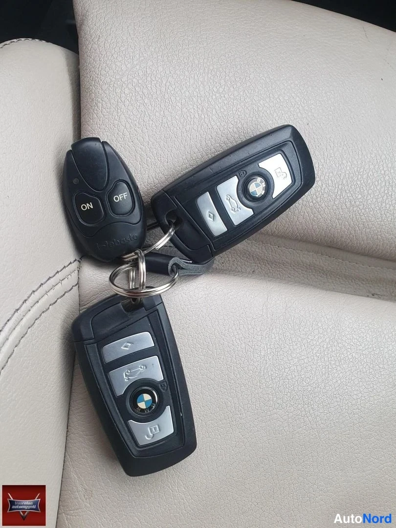 Yksityiskohta: Kolme avainetäohjainta beigeällä nahkapinnalla: kaksi BMW-avainta ja tumma lisäohjain ON- ja OFF-painikkeilla.