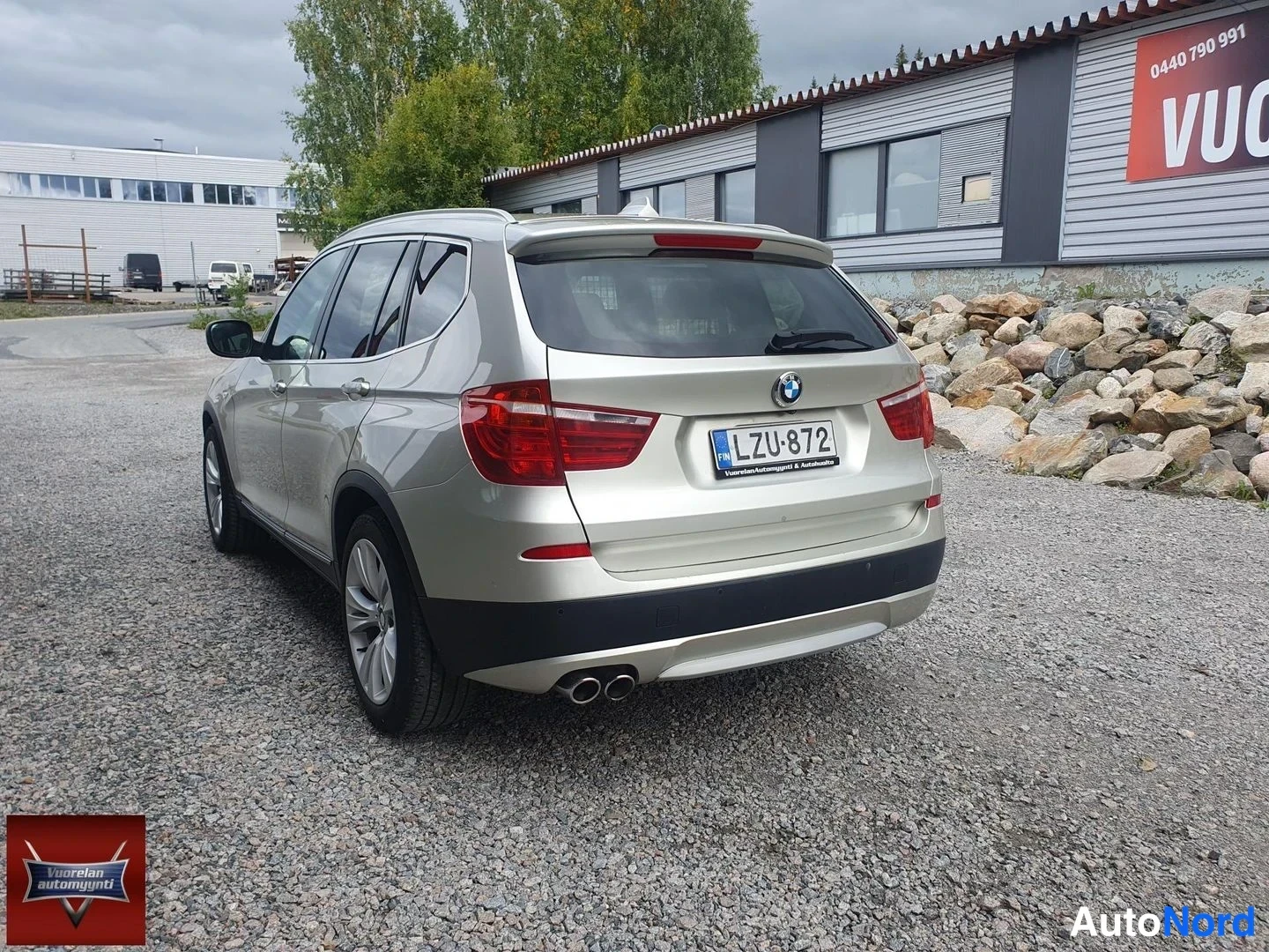 Takaviisto: BMW X3 kuvattu takaviistosta vasemmalta; kori on beigea metalliväriä, kaksoispakoputket ja rekisterikilpi näkyvät.
